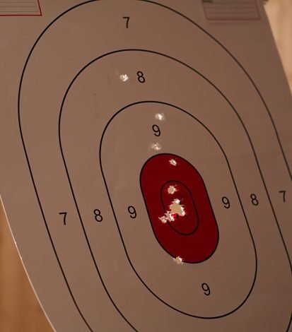 Man holding gun enjoying recreational indoor shooting, close up Man enjoying recreational shooting experience in firing range, checking if he shot bullseye. Person practicing with weapons in safe environment at shooting range company, hitting targets, camera B